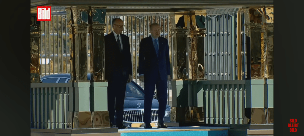 Merz (weiterhin nur optisch links) und Erdogan stehen unter einem Baldachin und lauschen der Hymne 