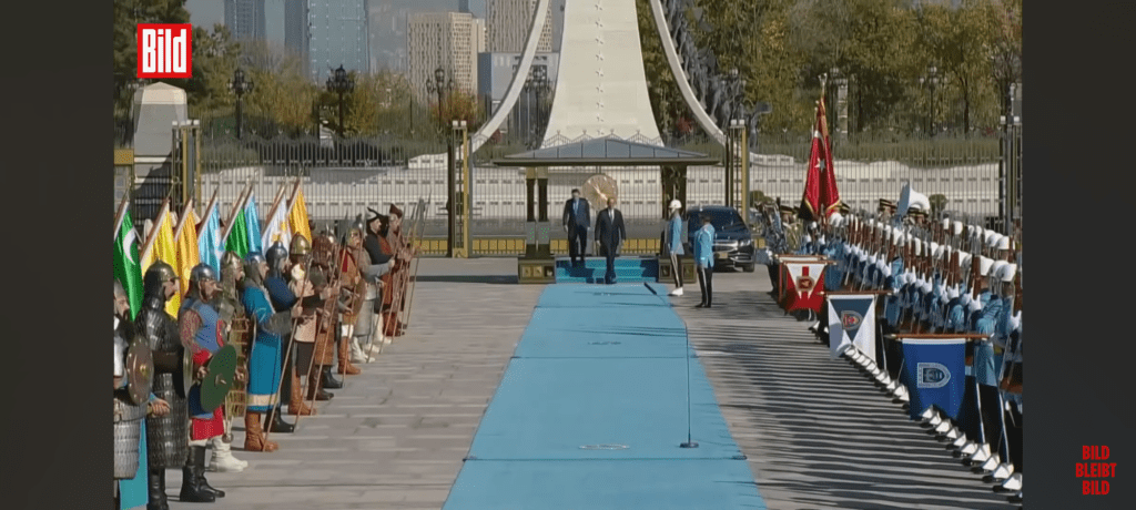 Merz (immer noch nur optisch links) und Erdogan verlassen das Podest mit dem Baldachin und betreten den hellblauen Staatsbesuchsteppich