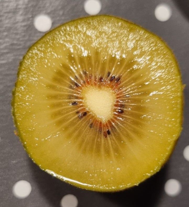 Vor dunkelgrauem Untergrund mit weißen Punkten siehst du eine aufgeschnittene Kiwi mit herzförmigem Inneren